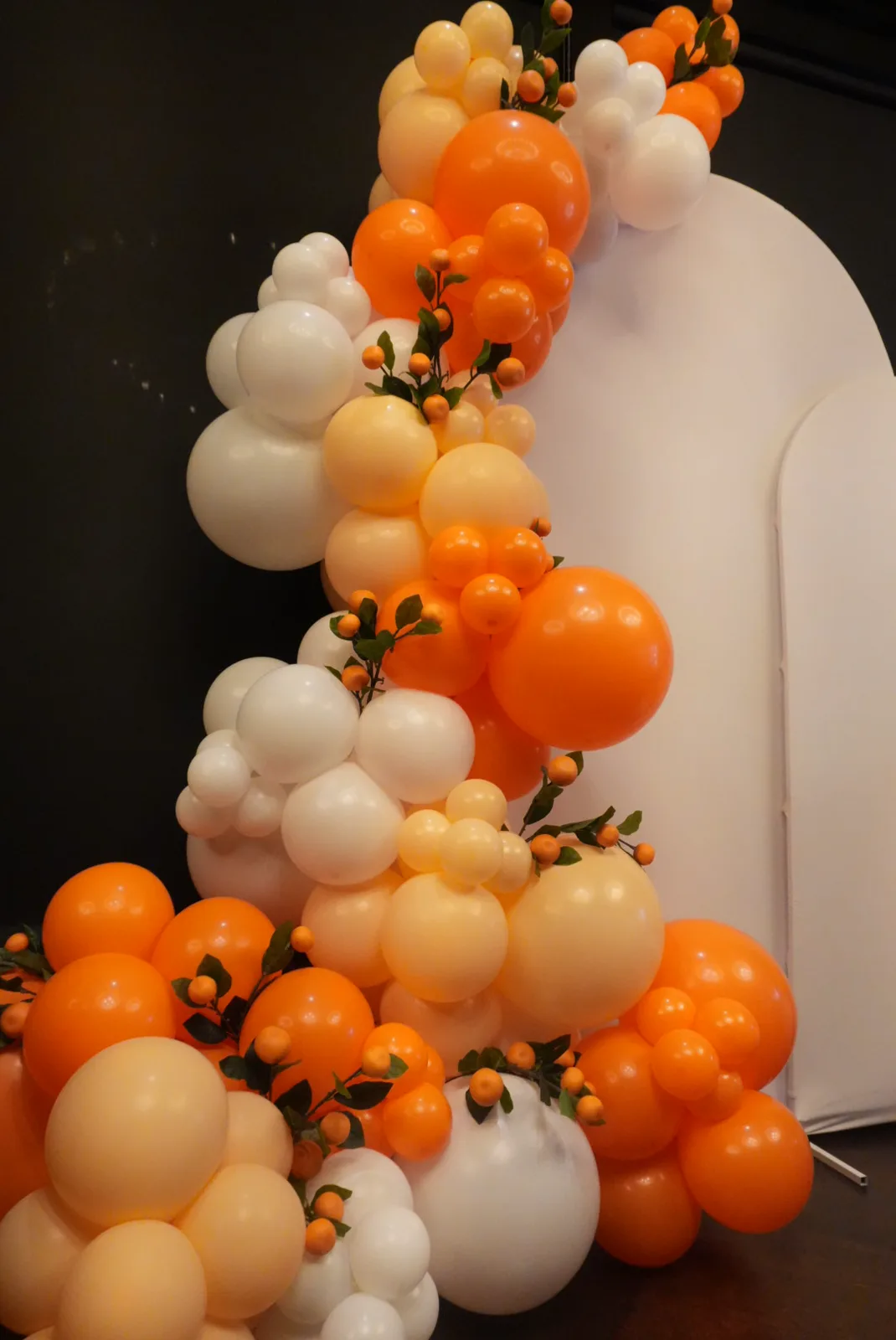 Orange and cream balloon garland with greenery on a cream arch backdrop